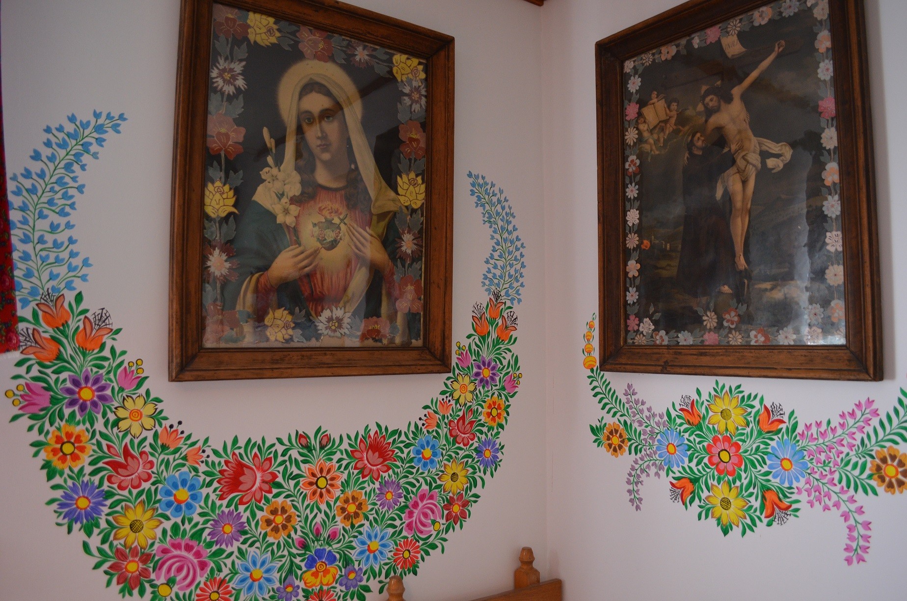 wnętrze domu, obrazy święte na ścianach otoczone kwiatowymi malunkami